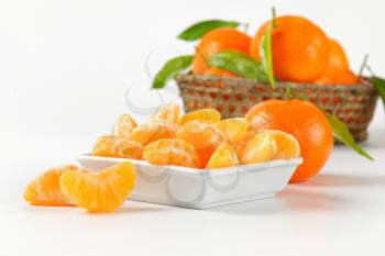 bowl of tangerine segments and whole tangerines on white background