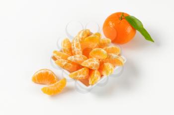 bowl of tangerine segments and whole tangerine on white background