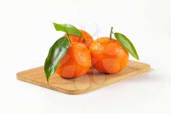 three tangerines with leaves on wooden cutting board