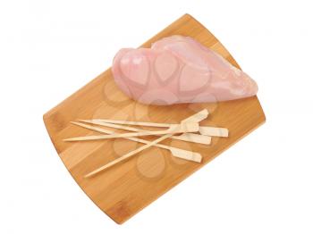raw chicken breast and wooden skewers on wooden cutting board
