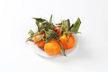 plate of fresh tangerines with leaves on white background