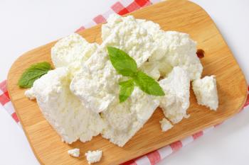 pile of crumbly white cheese on wooden cutting board