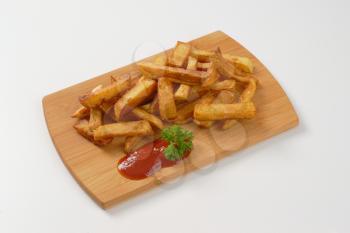 heap of fried chipped potatoes with ketchup on wooden cutting board