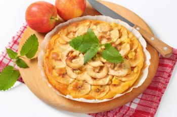 apple tart and fresh apples on round wooden cutting board