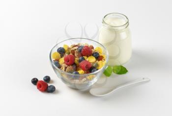 bowl of mixed breakfast cereals with fresh raspberries and blueberries, and jar of yogurt