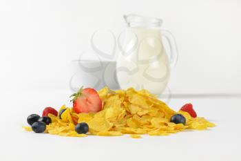 jug of milk and corn flakes with berry fruits on white background