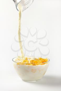 milk pouring into bowl of corn flakes on on off-white background with shadows