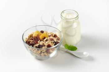 bowl of oat flakes with raisins and jar of white yogurt on off-white background