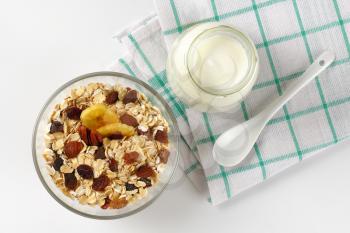 bowl of oat flakes and glass of white yogurt on checkered dishtowel