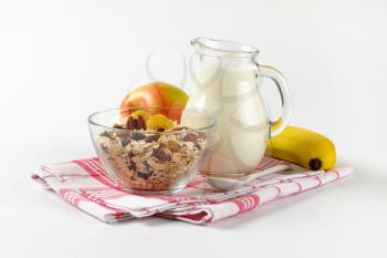 bowl of oat flakes, jug of milk and fruit on checkered dishtowel
