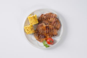 grilled pork meat steaks and corn on the cob on white plate