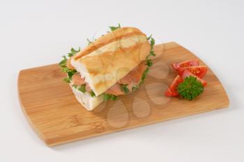 French bread sandwich with smoked salmon on wooden cutting board
