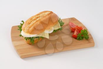 crusty roll sandwich with eggs and cheese on wooden cutting board