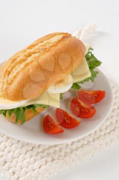 crusty roll sandwich with eggs and cheese on white plate