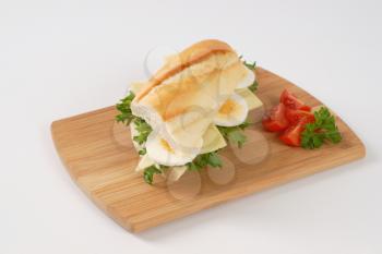 French bread sandwich with eggs and cheese on wooden cutting board