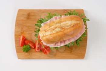 crusty roll sandwich with ham on wooden cutting board