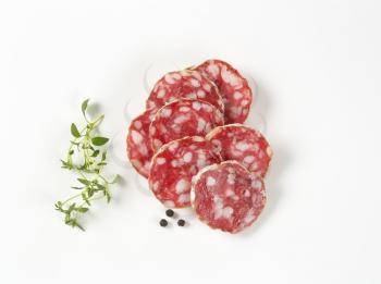 thin slices of dry cured sausage, thyme and peppercorns on white background