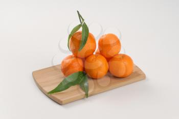 stack of fresh tangerines with leaves on wooden cutting board