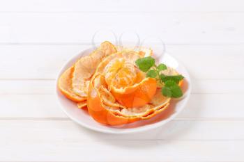 peeled tangerine arranged in peels on white plate