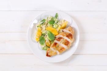 roasted chicken breast with rice and oranges on white plate