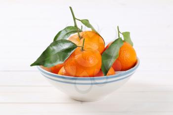 bowl of fresh tangerines with leaves on white background