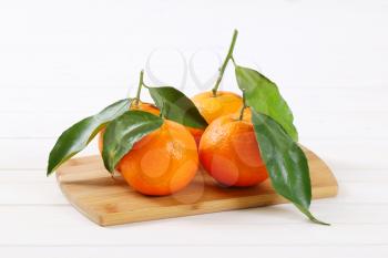 fresh tangerines with leaves on wooden cutting board