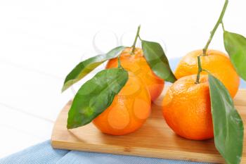 fresh tangerines with leaves on wooden cutting board - close up
