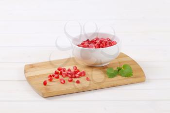 bowl of pomegranate seeds on wooden cutting board