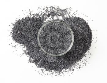 Whole black poppy seeds in glass bowl and around it