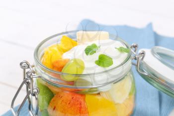 jar of fresh fruit salad with white yogurt on blue place mat - close up
