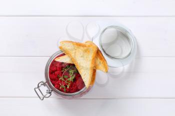 jar of fresh beetroot puree with toast on white wooden background