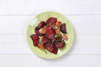 plate of baked beetroot with garlic and thyme on white wooden background