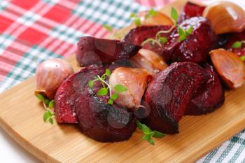 pile of baked beetroot with garlic and thyme on wooden cutting board - close up