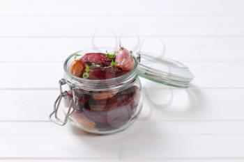 jar of baked beetroot with garlic and thyme on white wooden background