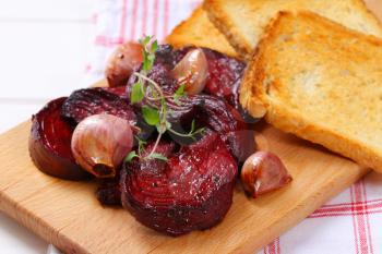 baked beetroot and garlic with toasted bread on wooden cutting board - close up