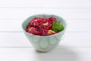 bowl of fresh beetroot spread with walnuts on white wooden background