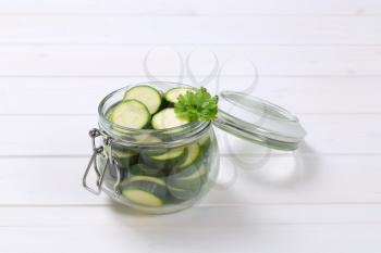 jar of green zucchini slices on white wooden background