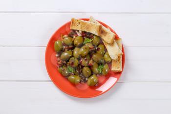 plate of marinated green olives with toast on white wooden background