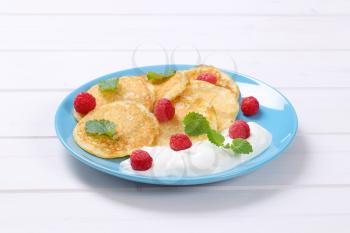 plate of american pancakes with white yogurt and fresh raspberries on white wooden background