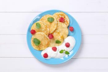 plate of american pancakes with white yogurt and fresh raspberries on white wooden background