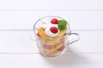 cup of american pancakes with white yogurt and fresh raspberries on white wooden background