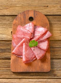 thin slices of spicy salami folded on wooden cutting board