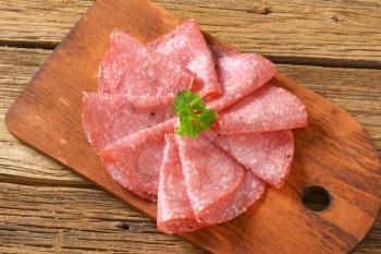 thin slices of spicy salami folded on wooden cutting board