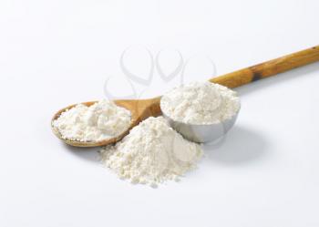 soft wheat flour on wooden spoon and in metal bowl on white background