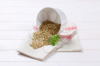 bowl of dry brown lentils spilt out on white dishtowel