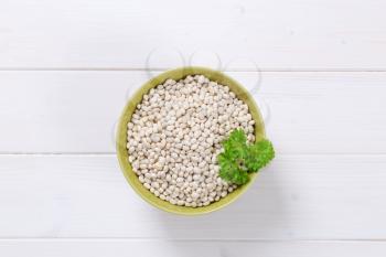 bowl of raw white beans on white wooden background