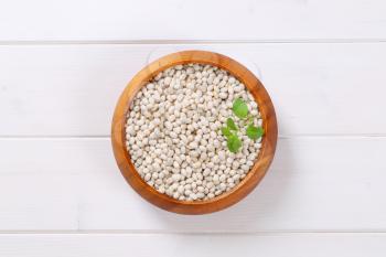 bowl of raw white beans on white wooden background