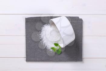 bowl of coarse grained sea salt spilt out on grey place mat