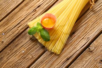 Dried spaghetti and raw egg on wooden background