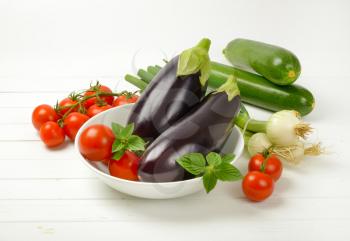 fresh eggplants, tomatoes, zucchini and spring onion on white wooden background